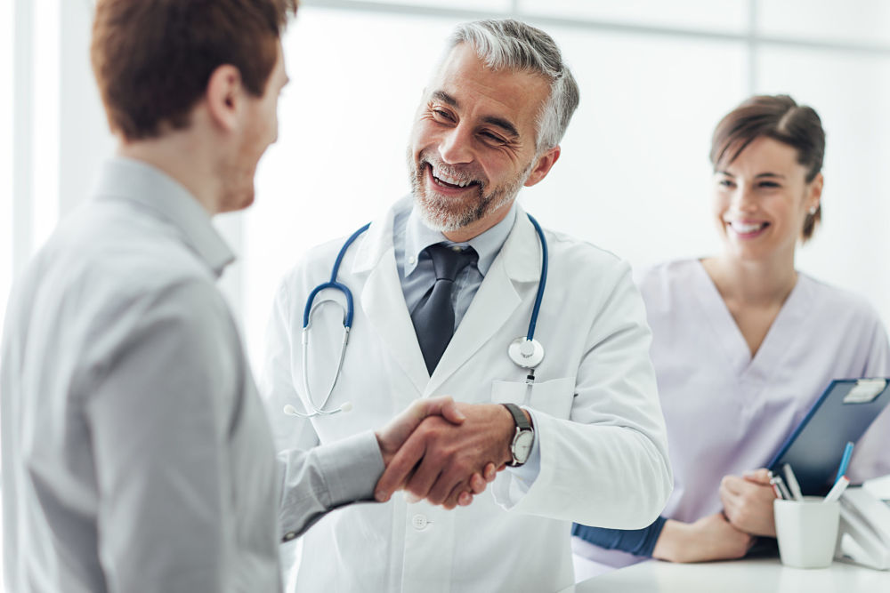 Smiling doctor at the clinic giving an handshake to his patient, healthcare and professionalism concept